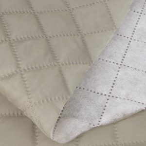 May include: A close-up of a beige quilted fabric with a white quilted backing. The fabric has a diamond pattern with small dots along the stitching.