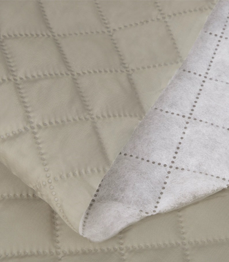 May include: A close-up of a beige quilted fabric with a white quilted backing. The fabric has a diamond pattern with small dots along the stitching.
