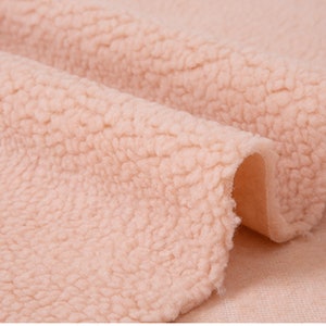 May include: Close-up of a soft, pale pink faux fur fabric. The fabric has a fluffy, textured surface.