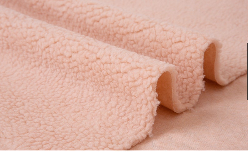May include: Close-up of a soft, pale pink faux fur fabric. The fabric has a fluffy, textured surface.
