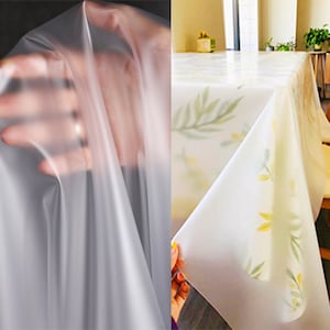 May include: Clear plastic tablecloth with a floral pattern. The tablecloth has a white background with green leaves and yellow flowers.