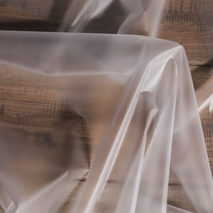 May include: A clear plastic tablecloth draped over a wooden surface. The tablecloth is smooth and has a slight sheen.