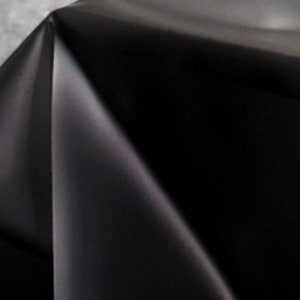 May include: A close-up of a black fabric with a smooth, silky texture. The fabric is folded in a way that creates a soft, flowing drape.