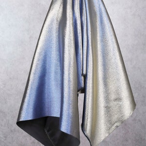 May include: A silver and blue fabric with a shimmery finish. The fabric is draped over a surface and has a soft, flowing texture.