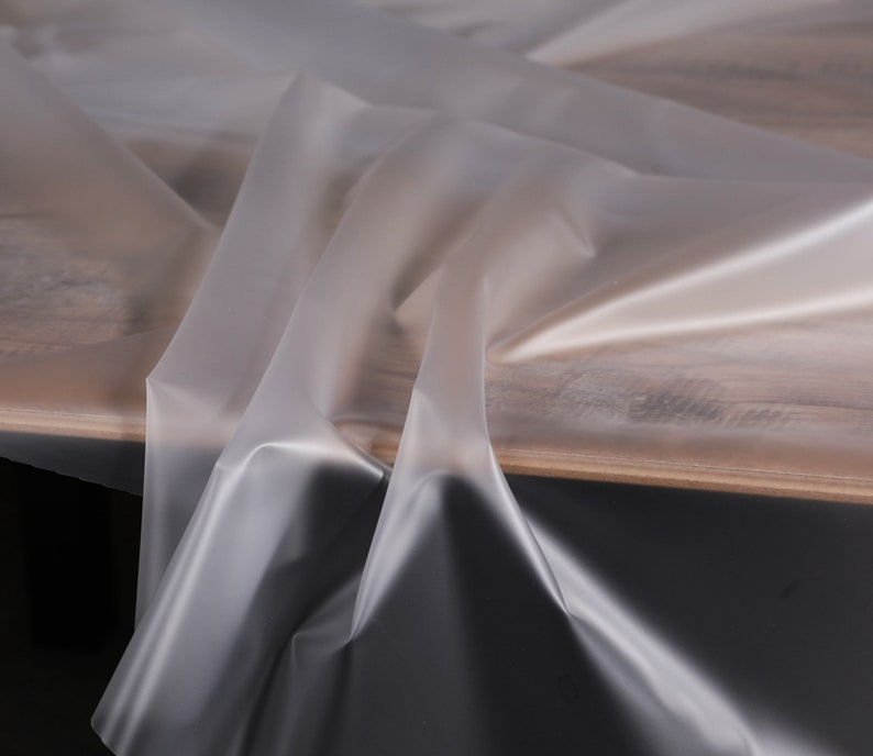 May include: A clear plastic tablecloth draped over a wooden table. The tablecloth is smooth and translucent, with a slight sheen.