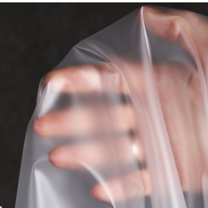 May include: A close-up of a clear, translucent plastic sheet. The sheet is smooth and has a slight sheen. The sheet is being held by a hand, but the hand is not visible.