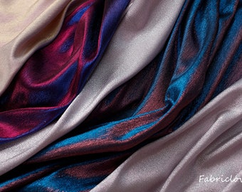 May include: Close-up of iridescent fabric in shades of teal, burgundy, and silver. The fabric is folded and draped, showcasing its shimmering texture.