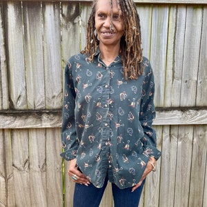 Pu&ograve; includere: Una camicia verde a maniche lunghe con bottoni e un motivo di piccoli ferri di cavallo marroni e bianchi. La camicia ha un colletto e una chiusura con bottoni sul davanti.
