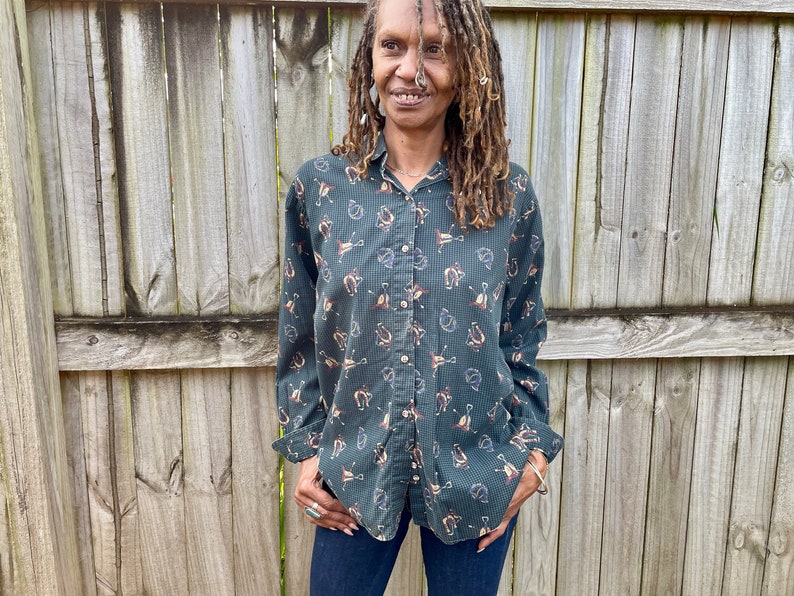 Pu&ograve; includere: Una camicia verde a maniche lunghe con bottoni e un motivo di piccoli ferri di cavallo marroni e bianchi. La camicia ha un colletto e una chiusura con bottoni sul davanti.