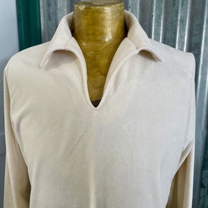 Puede incluir: Una camisa de manga larga de color crema con un cuello ancho en forma de V y un cuello.