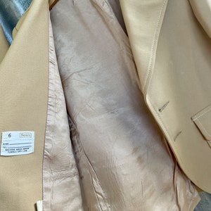 May include: A beige blazer with a pocket on the right side. The inside of the blazer is a light beige color. The label on the inside of the blazer says "Sears" and "6". The label also says "Machine Wash Warm, Tumble Dry Low."
