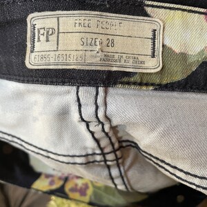 May include: A black and white tag with the text "Free People" and "Size: 28" on a pair of black jeans with a floral print.