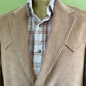 May include: A brown corduroy blazer with a plaid shirt underneath. The blazer has a notched lapel and two flap pockets.