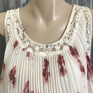 Puede incluir: Una blusa blanca sin mangas con estampado floral y un ribete de encaje alrededor del escote.