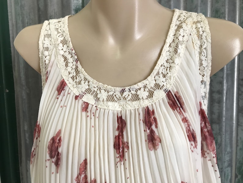 Puede incluir: Una blusa blanca sin mangas con estampado floral y un ribete de encaje alrededor del escote.