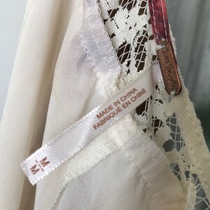 Puede incluir: Borde de encaje blanco en un vestido blanco con una etiqueta de Free People y una etiqueta de talla M. La etiqueta dice "Made in China, Fabrique en Chine".