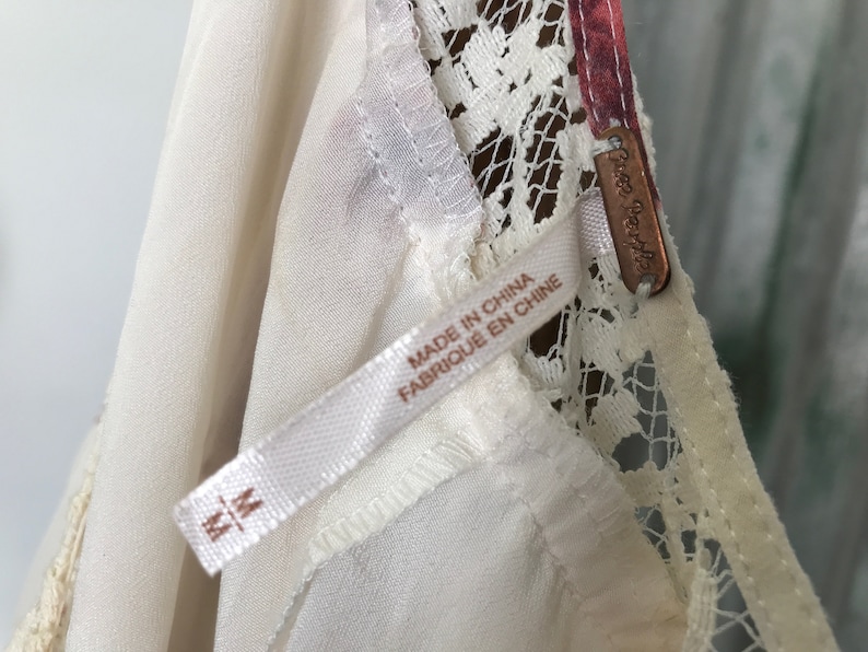 Puede incluir: Borde de encaje blanco en un vestido blanco con una etiqueta de Free People y una etiqueta de talla M. La etiqueta dice "Made in China, Fabrique en Chine".