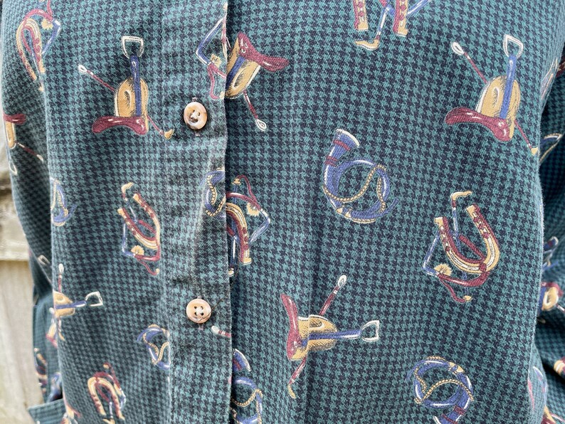 Pu&ograve; includere: Una camicia verde e nera con bottoni, con un motivo pied-de-poule e un motivo ripetuto di immagini equestri, tra cui selle, staffe e briglie.