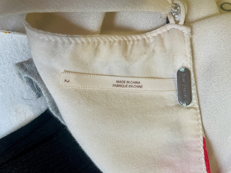 May include: A white garment with a label that reads "Made in China Fabrique en Chine" and a size tag that says "2". The garment also has a small metal tag that says "Free People".