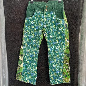 May include: Green corduroy trousers with a floral print. The trousers have a wide leg and a high waist.