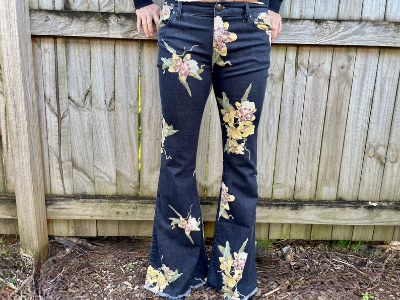 May include: Black flared jeans with a floral print featuring yellow and pink flowers.