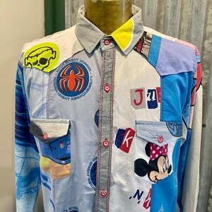 May include: A patchwork button-down shirt with a gray collar and yellow accent. The shirt features various patches, including a Spider-Man logo, a skull, and a Minnie Mouse graphic. The shirt has two front pockets and red stitching.