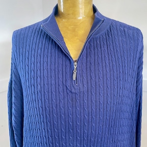 Op de afbeelding: Een marineblauwe kabelgebreide trui met een kwartrits. De trui heeft een geribbelde kraag en manchetten. De rits is zilverkleurig. Het materiaal is zacht en getextureerd. Klassieke en veelzijdige stijl.