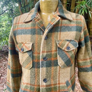 Puede incluir: Chaqueta a cuadros en tonos beige, verde y naranja con dos bolsillos en el pecho y cierre de botones. La chaqueta tiene cuello y botones oscuros. La tela parece ser lana gruesa o una mezcla de lana.