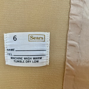 May include: White label with the text "Sears" and the number "6" printed on it. The label also includes the text "Name", "Tel", "Machine Wash Warm", and "Tumble Dry Low".