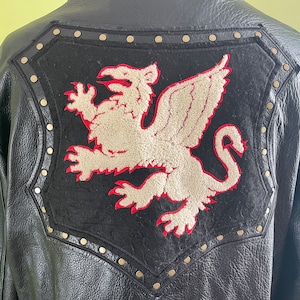 May include: Black leather jacket with a large, black, felt patch on the back. The patch features a white, embroidered griffin with red accents.