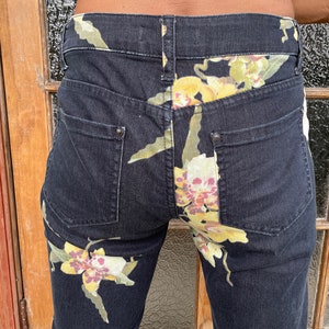 May include: Black denim jeans with a floral print of yellow, white, and pink orchids.