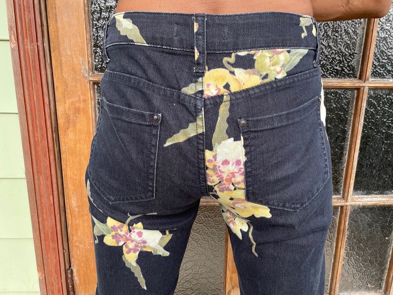 May include: Black denim jeans with a floral print of yellow, white, and pink orchids.