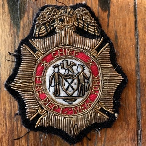 Puede incluir: Un parche bordado en oro y rojo con las palabras "Chief Fire Dept. New York" y un águila estilizada arriba.