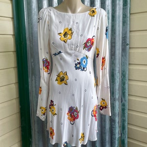 May include: White mini dress with a floral print and a scoop neck. The dress has long sleeves with a gathered cuff detail.