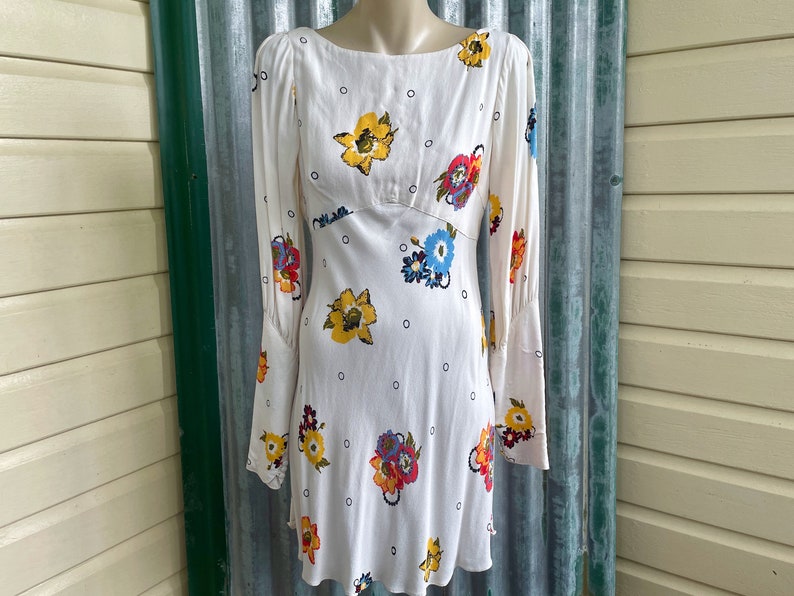 May include: White mini dress with a floral print and a scoop neck. The dress has long sleeves with a gathered cuff detail.