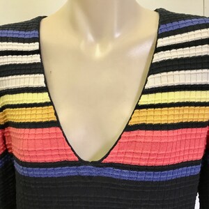 Puede incluir: Un su&eacute;ter de rayas blancas y negras con rayas horizontales de colores en tonos azules, amarillos, naranjas y rosas. El su&eacute;ter tiene un cuello en V.