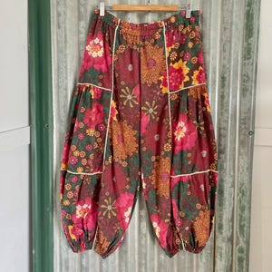 Può includere: Un paio di pantaloni a gamba larga con stampa floreale rosso e marrone, vita elastica e orlo arricciato.