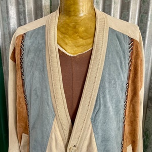 May include: A beige cardigan with a blue and brown suede panel design. The cardigan has a button closure and a V-neck.