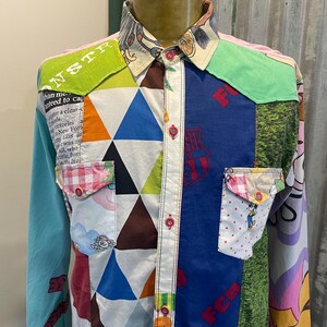 May include: A colourful patchwork long-sleeved shirt with a variety of patterns. The shirt features geometric shapes, text, and cartoon characters. The collar and cuffs have unique designs, and the shirt has two chest pockets.