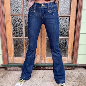 May include: A pair of dark blue denim jeans with a wide leg flare. The jeans have a high waist and a gold button and zipper closure.