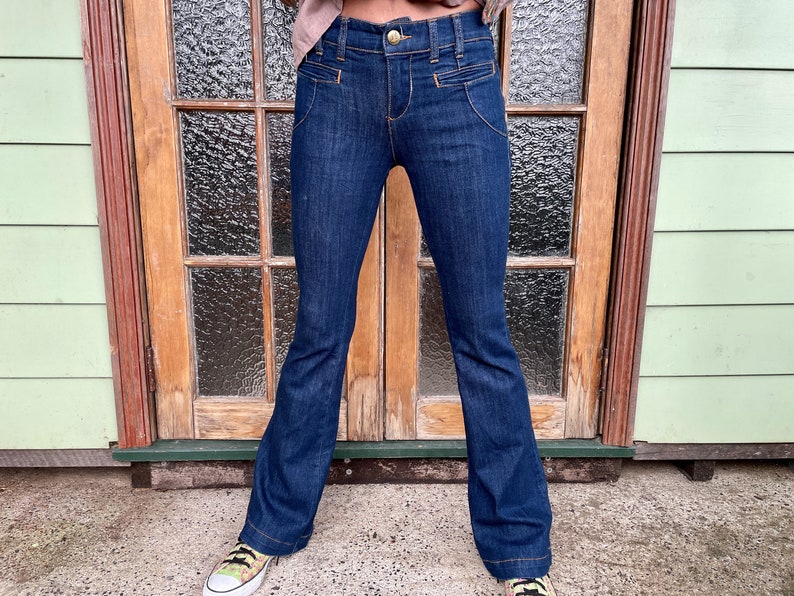 May include: A pair of dark blue denim jeans with a wide leg flare. The jeans have a high waist and a gold button and zipper closure.