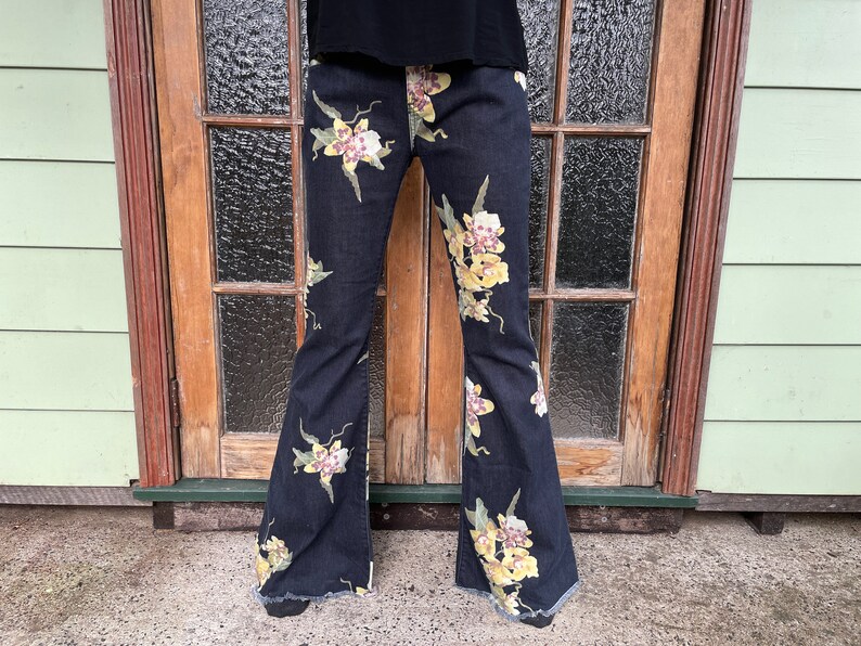 May include: Black flared jeans with a floral print of yellow and pink orchids.