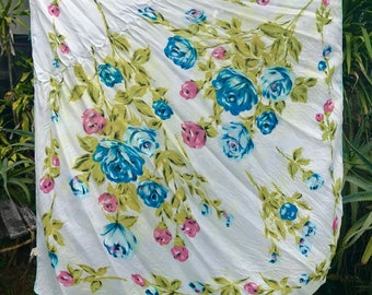 May include: White tablecloth with a floral pattern featuring blue and pink roses on green stems. The tablecloth is made of a lightweight fabric and has a slightly distressed look.