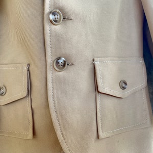 May include: A beige blazer with two flap pockets and three buttons. The pockets have white stitching around the edges.