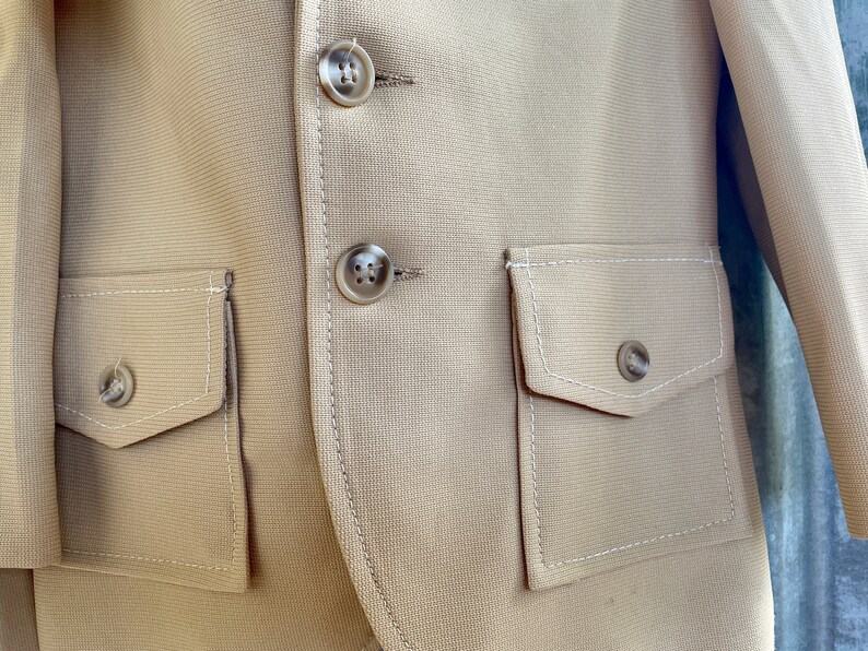 May include: A beige blazer with two flap pockets and three buttons. The pockets have white stitching around the edges.