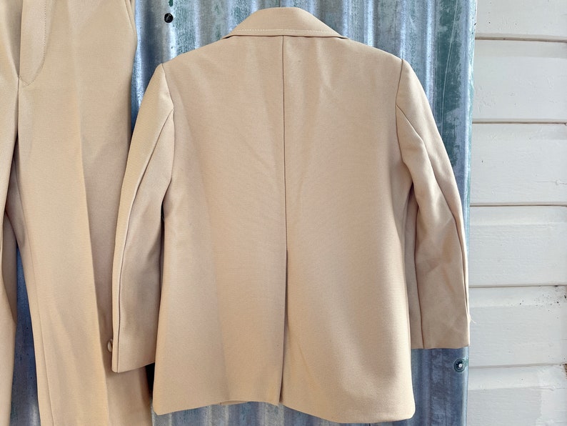 May include: A beige blazer with long sleeves and a single back vent. The blazer is made of a smooth, textured fabric.