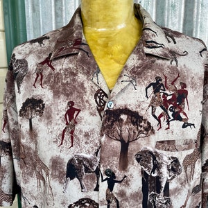 Op de afbeelding: Een beige overhemd met knopen en een safariprint met giraffen, olifanten en gestileerde figuren van mensen in een jungle-omgeving.