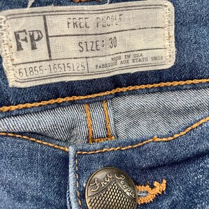 May include: A close-up of a pair of blue denim jeans with a brown leather patch that says "Free People" and a size tag that says "SIZE: 30".