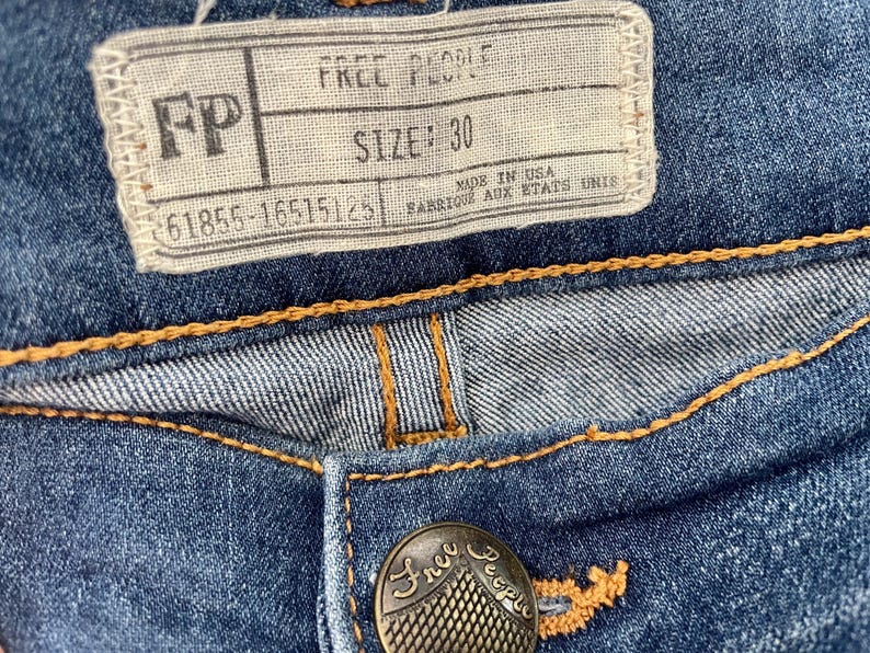 May include: A close-up of a pair of blue denim jeans with a brown leather patch that says "Free People" and a size tag that says "SIZE: 30".
