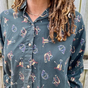 Pu&ograve; includere: Una camicia a maniche lunghe abbottonata a quadri verdi e bianchi con una stampa di cavallo e ferro di cavallo.